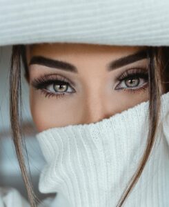 Portrait of a woman with striking eye makeup wearing a cozy white turtleneck sweater indoors.